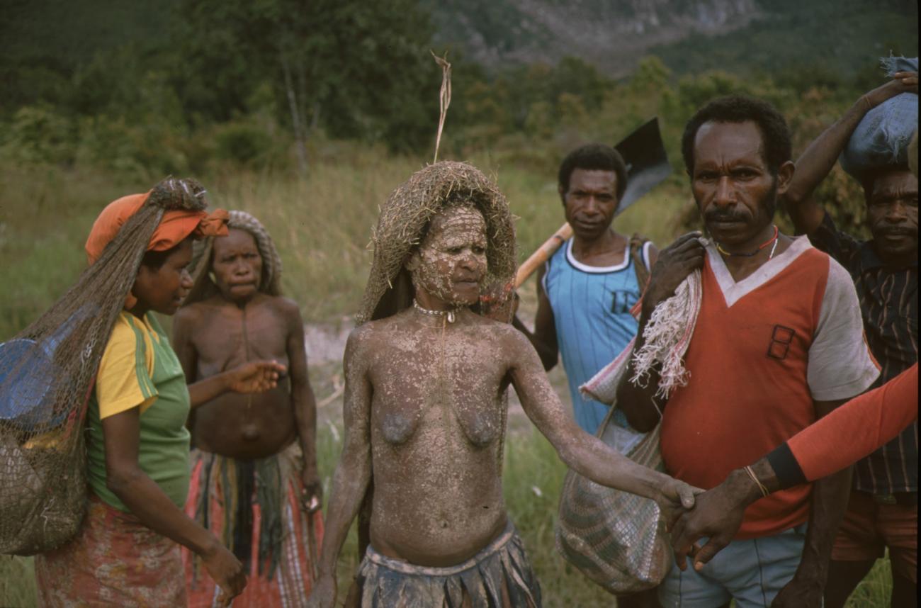 BD/166/166 - 
Vrouw met witte vlekken [modder] wordt omringd door mensen.
