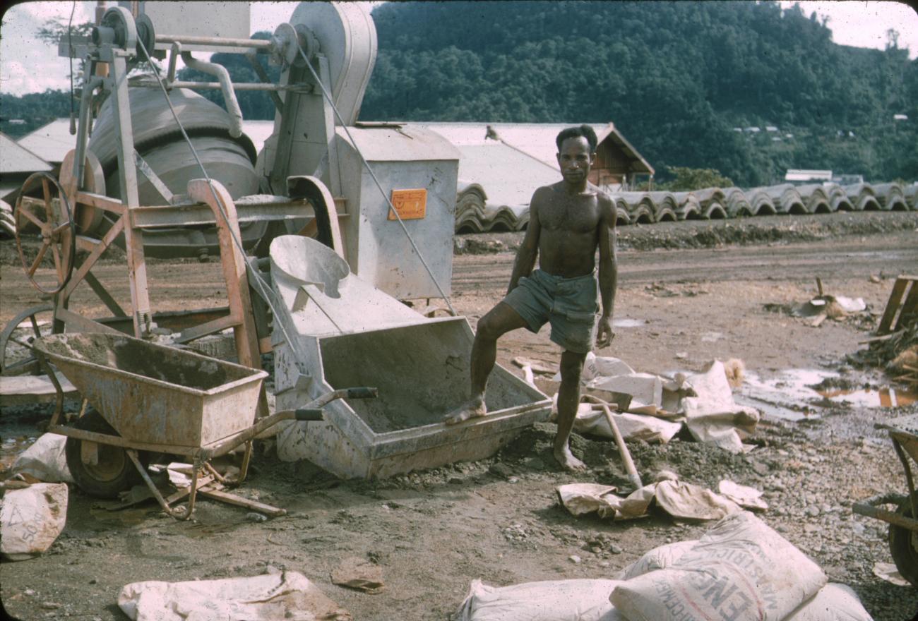 BD/288/17 - 
Man poseert voor stortbak van cementmolen, bouw ziekenhuis VAM
