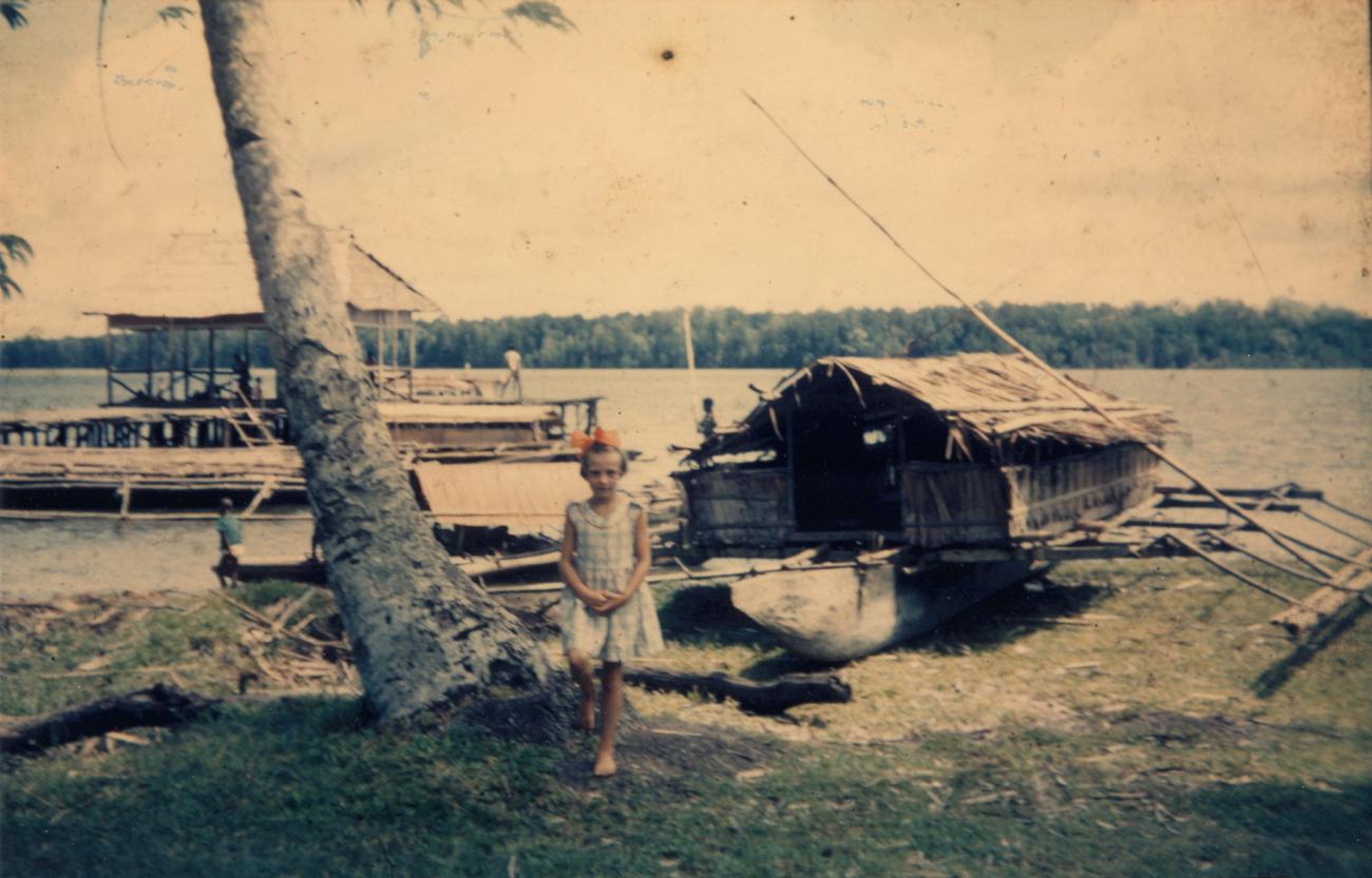 BD/309/35 - 
Dorp Konda, westers meisje met op achtergrond vlerkprauw op de kant en baai
