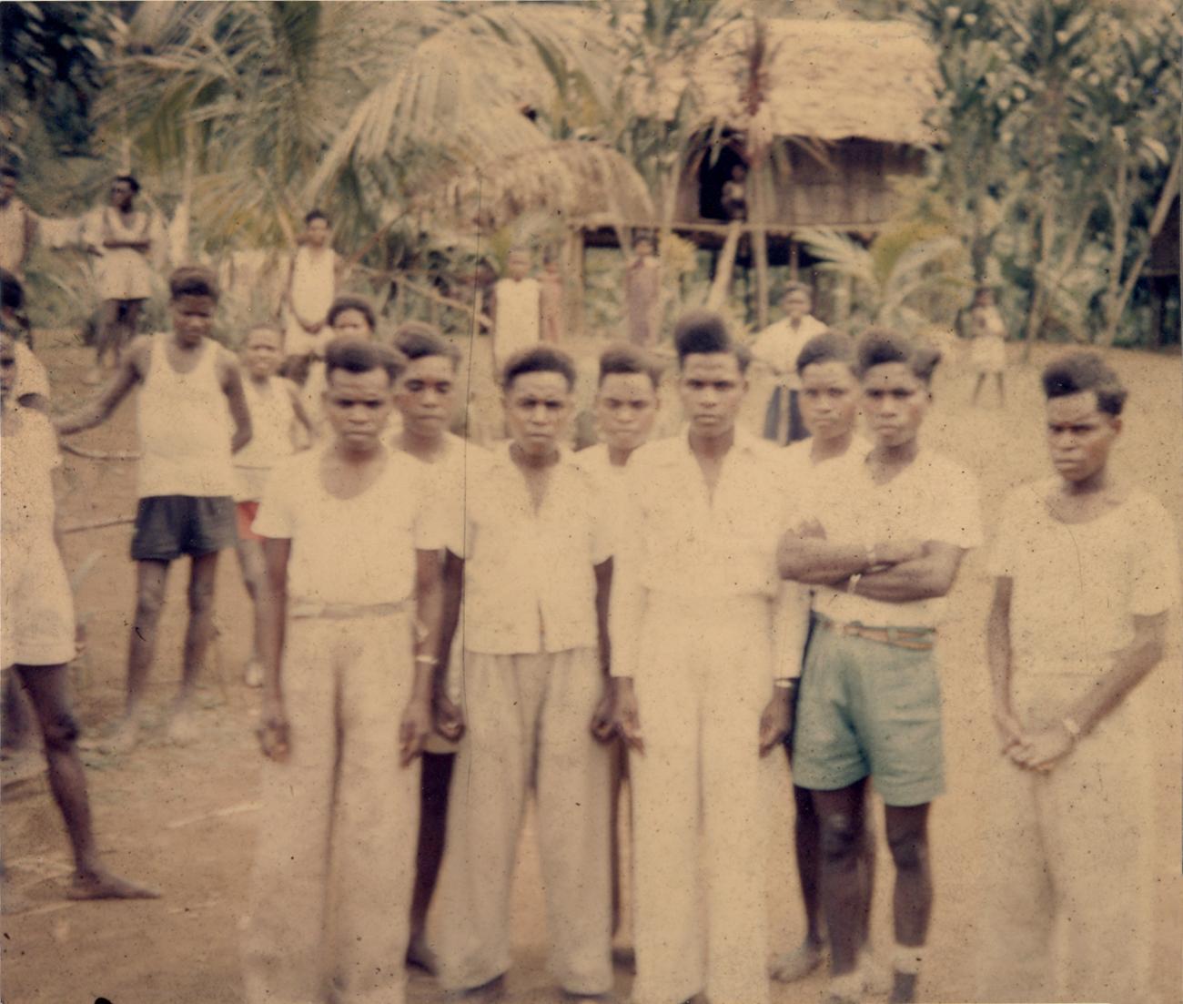 BD/309/37 - 
Dorp Sosenek, groepsfoto van jonge mannen met op achtergrond paalwoning
