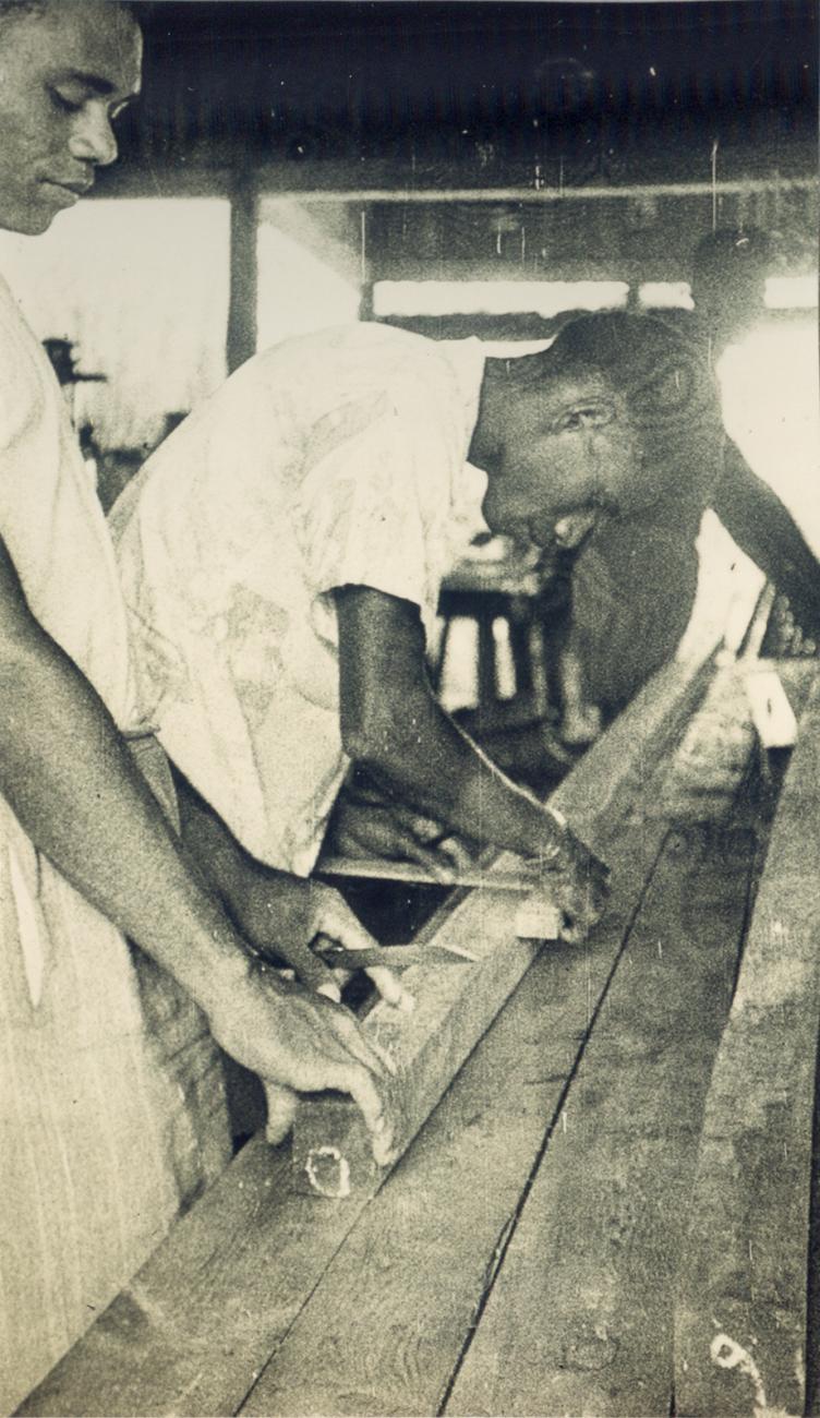 BD/309/64 - 
Dorp Teminabuan, mannen bezig met houtbewerking
