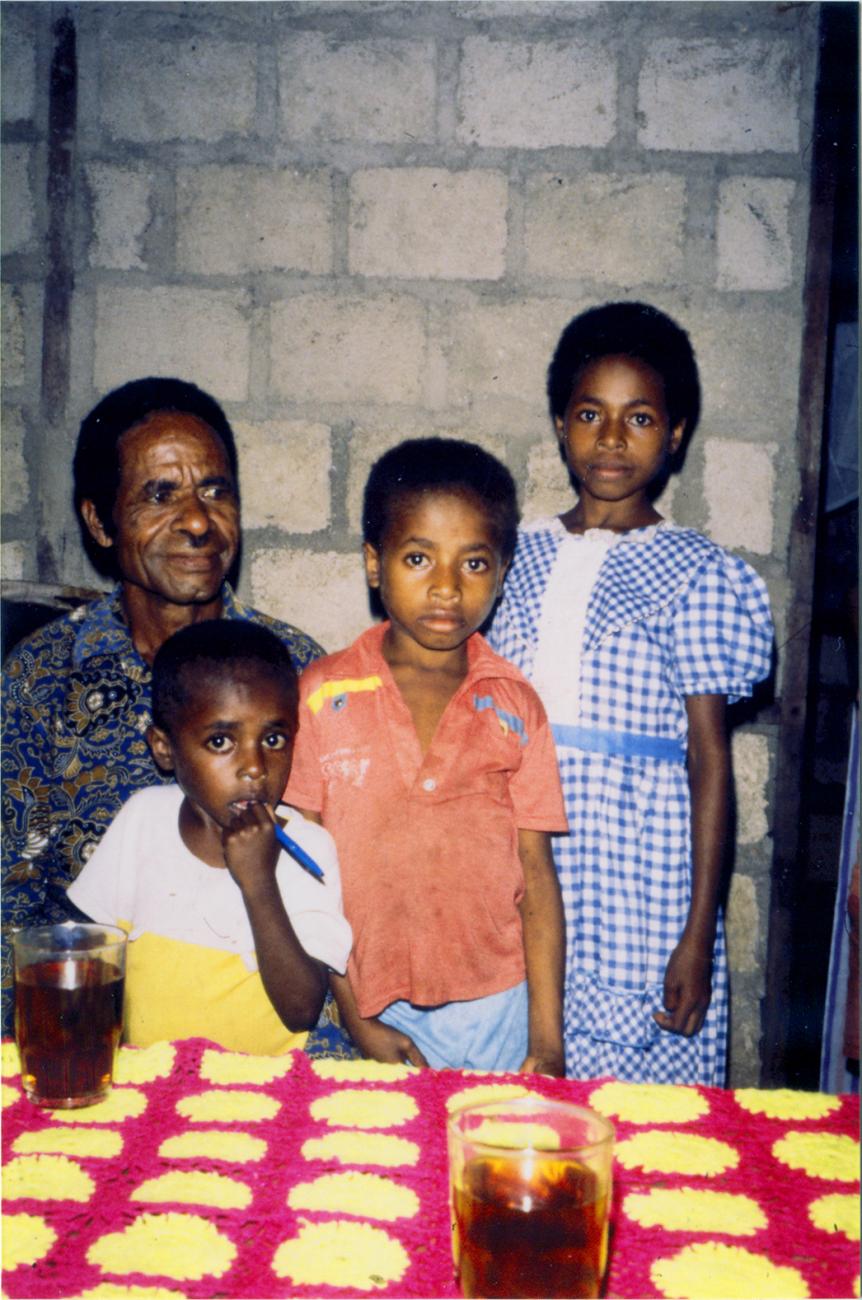 BD/309/72 - 
Dorp Teminabuan, man met kinderen bij tafel met limonade  
