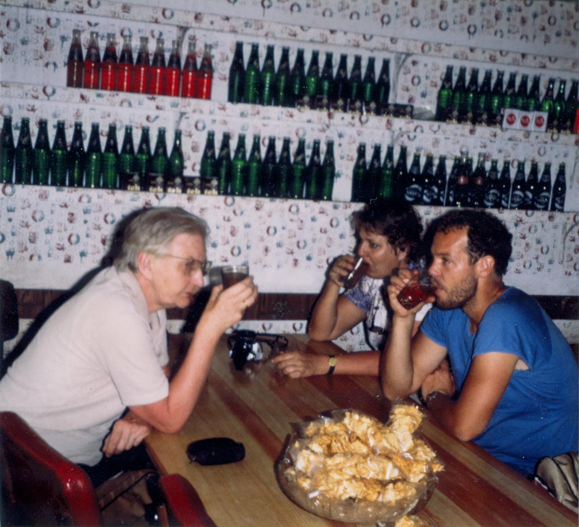 BD/309/75 - 
Dorp Bogor, westerse oudere man en jonge man en vrouw drinken wat in gelegenheid. Niet plaatsen, niet in Nieuw Guinea
