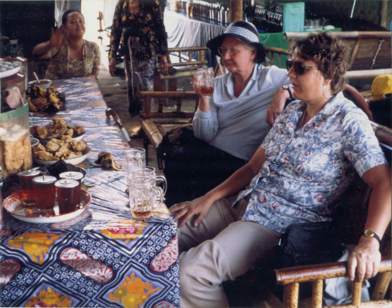 BD/309/76 - 
Dorp Bogor, westerse jonge en wat oudere vrouw aan de maaltijd. Niet plaatsen, niet in Nieuw Guinea 
