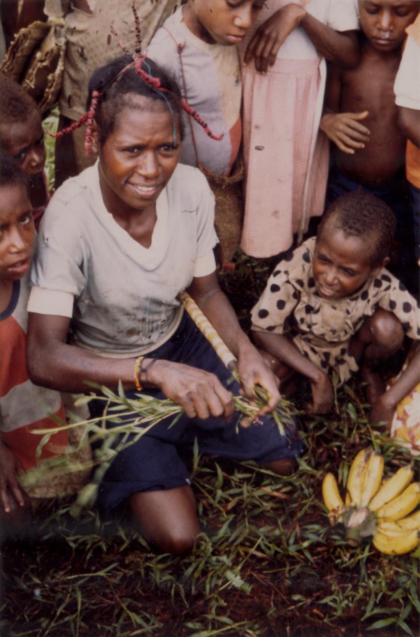 BD/309/82 - 
Dorp Bogor, vrouw omringd door kinderen op markt. Niet publiceren, niet in Nieuw Guinea 
