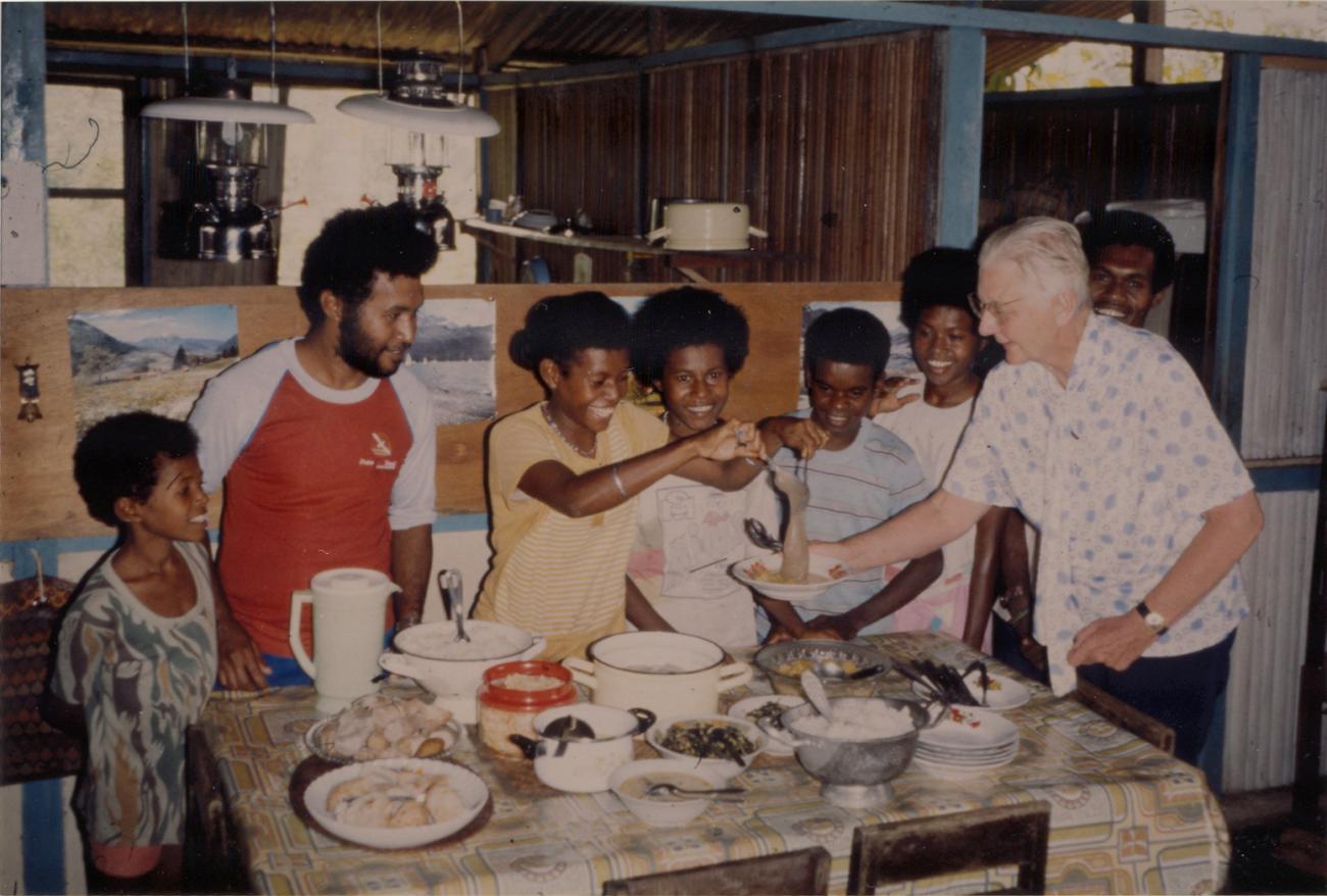 BD/309/85 - 
Dorp Bogor, etenstijd, maaltijd wordt opgediend. Niet publiceren, niet in Nieuw Guinea
