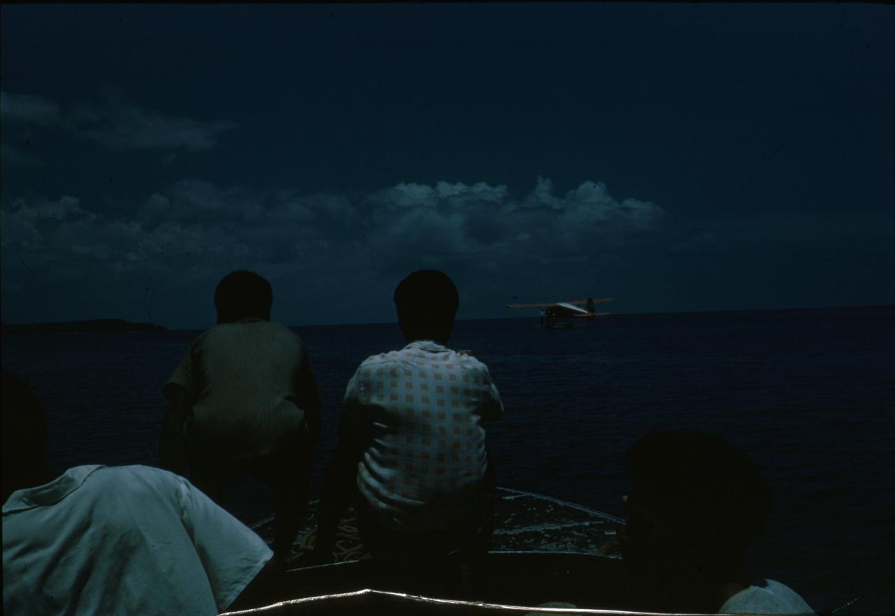 BD/144/18 - 
Twee papoea&#039;s op rug gezien, watervliegtuig op achtergrond
