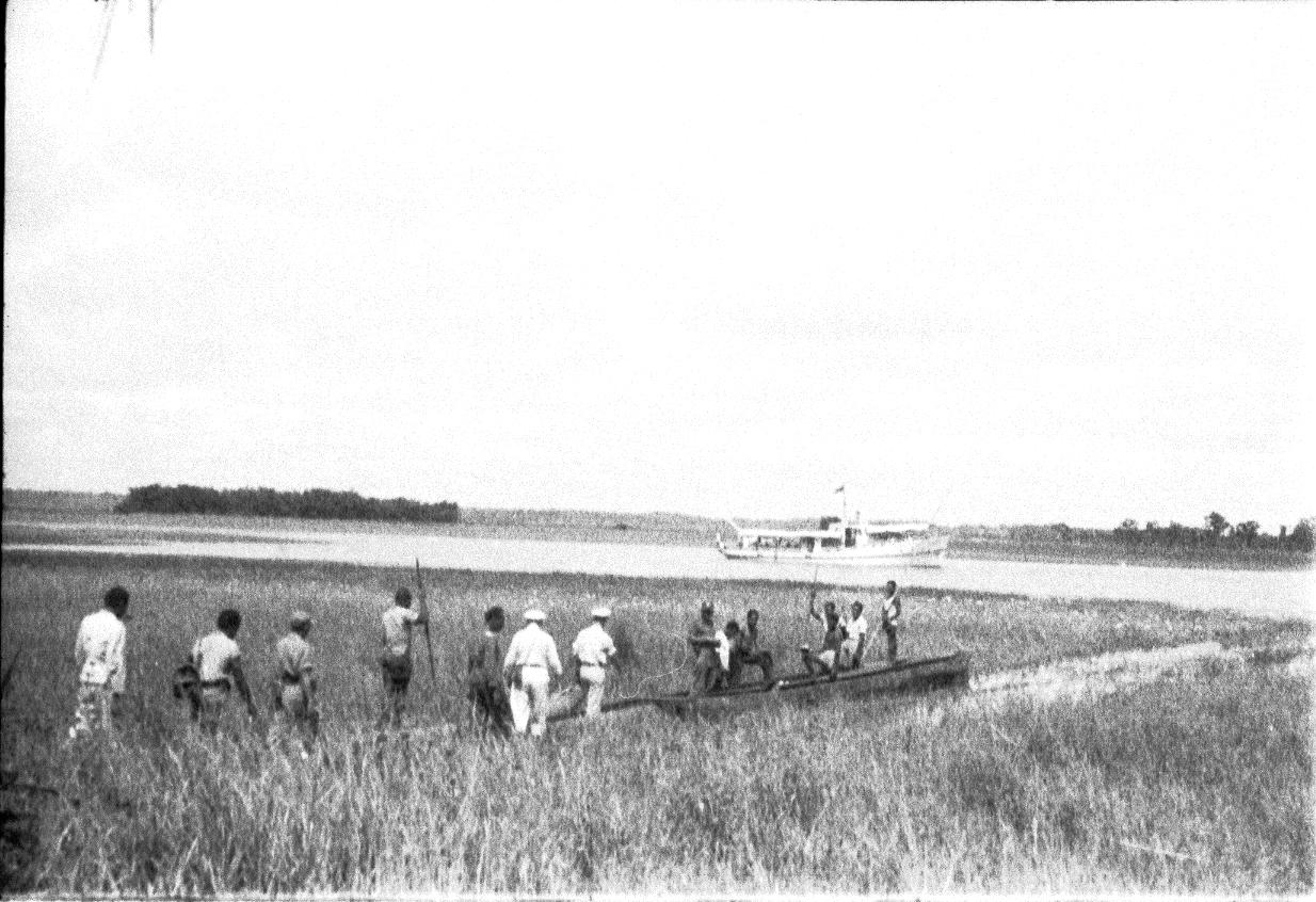 BD/67/235 - 
Mensen onderweg door het water, tussen het riet
