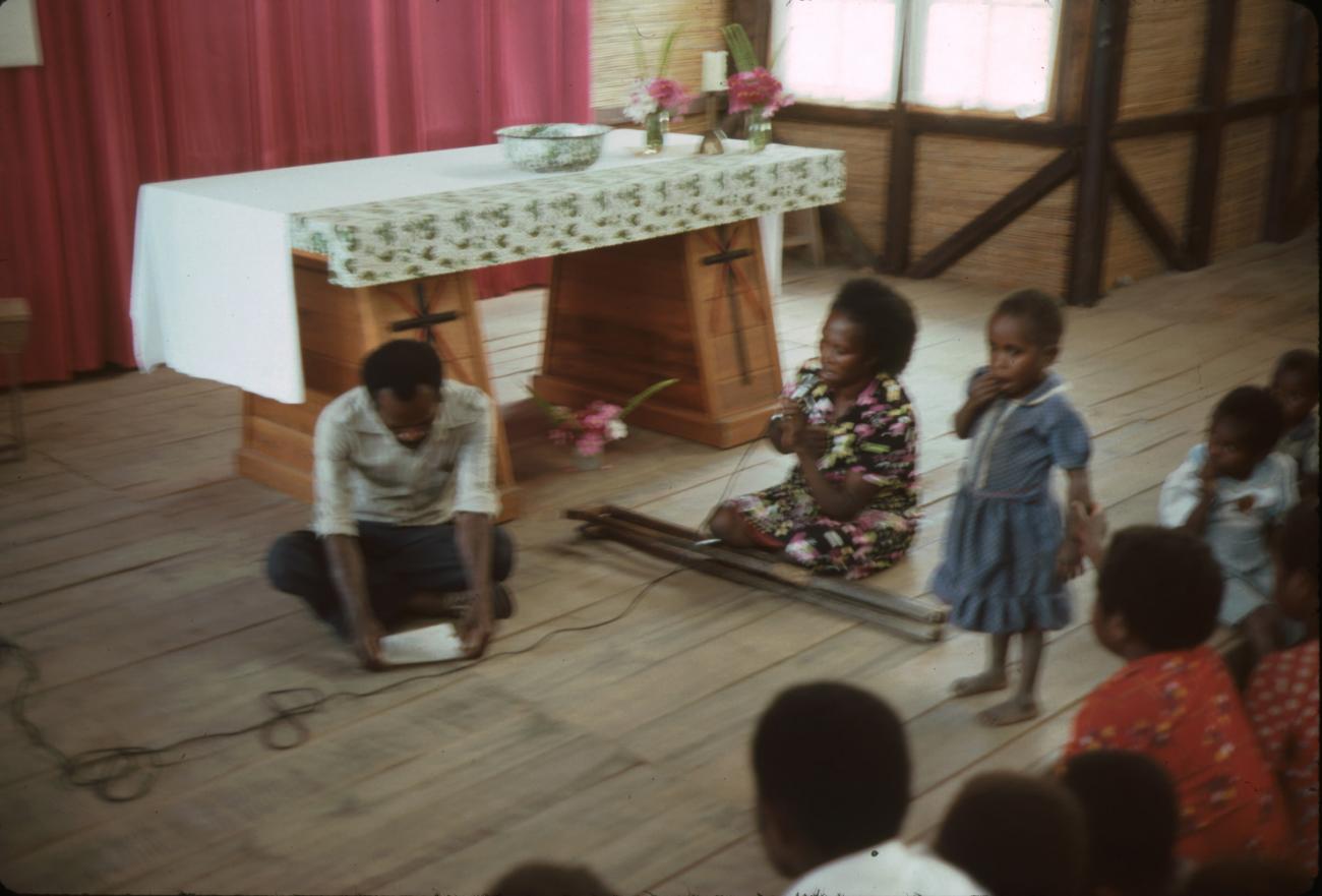 BD/132/16 - 
groepsfoto met man, vrouw en kinderen in kerk die iets voorlezen 
