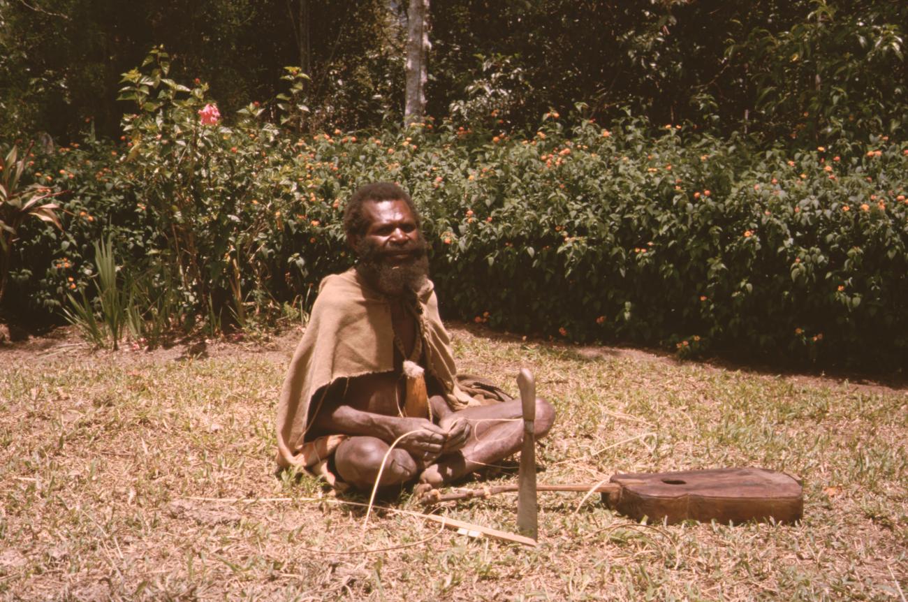 BD/132/173 - 
zittende Papua met peniskoker, machete en gitaar
