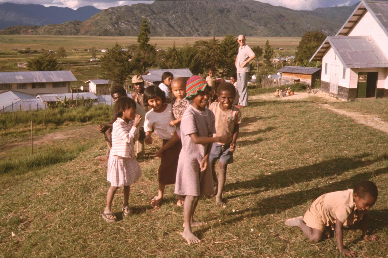 BD/132/22 - 
groepsfoto van man en kinderen met huizen op achtergrond
