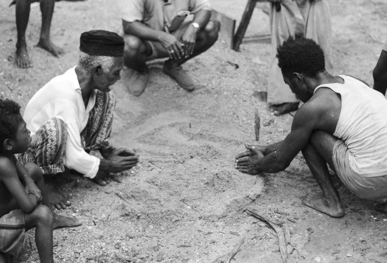BD/133/1180 - 
Papoea-mannen tekenen een kaart in het zand
