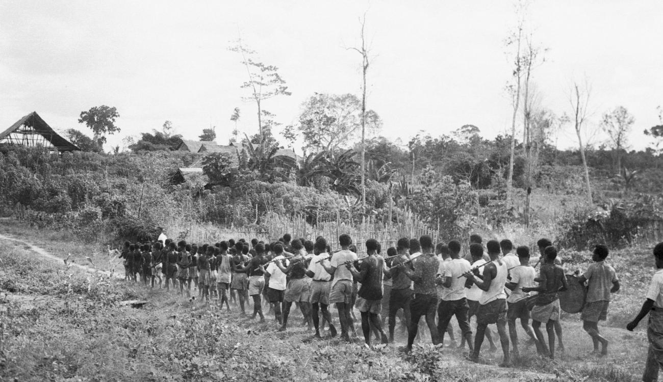 BD/133/180 - 
Een grote groep Papoea&#039;s (muziek????) onderweg
