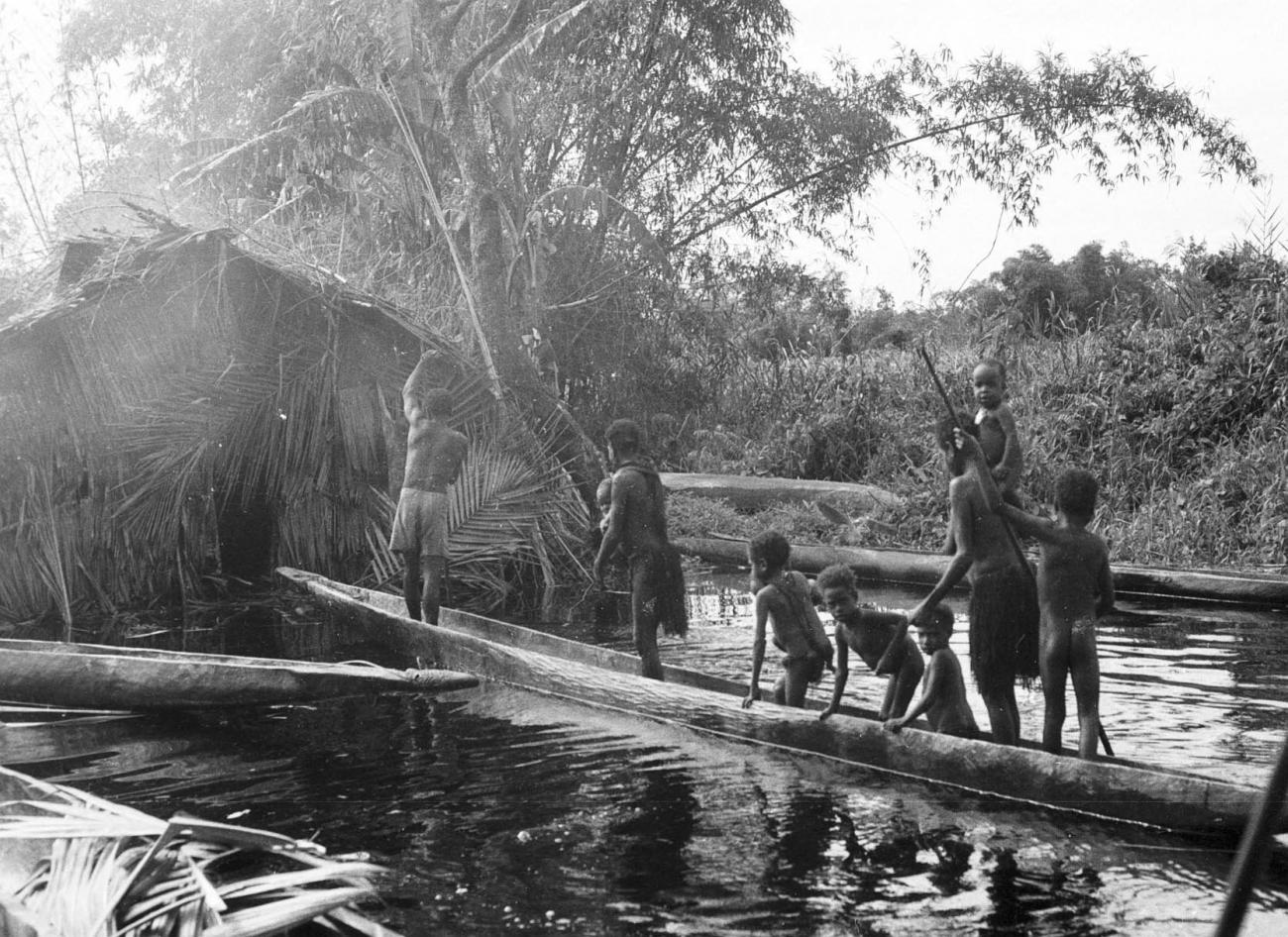 BD/133/299 - 
Tocht Merauke-Kepi-Cook: Marind-anim mensen in een prauw bij een hutje
