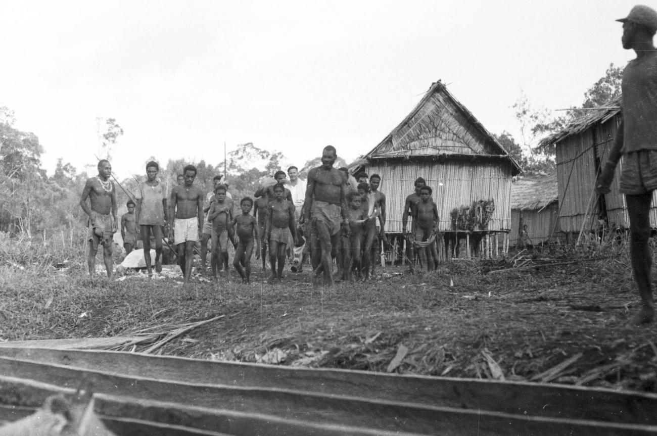 BD/133/445 - 
Tocht Merauke-Kepi-Cookrivier vv: Bevolking op oever voor een hut te Kepi
