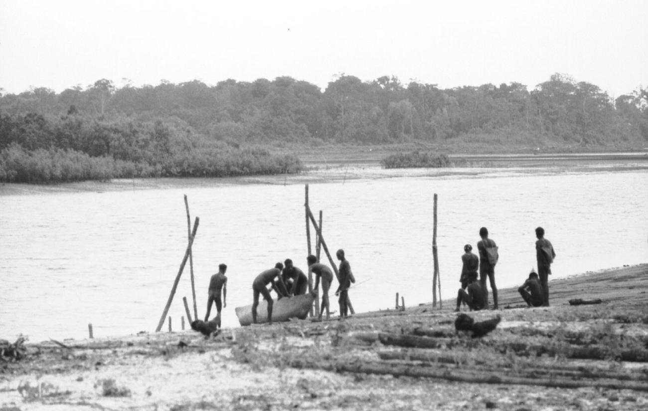 BD/133/65 - 
Tocht Merauke-Kapi: Mannen met boot aan de rivier
