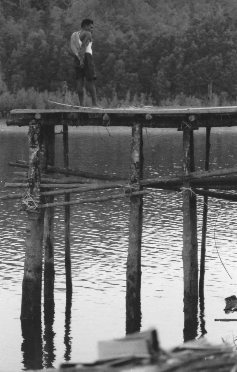 BD/133/66 - 
Tocht Merauke-Kapi: Man op steiger aan de rivier
