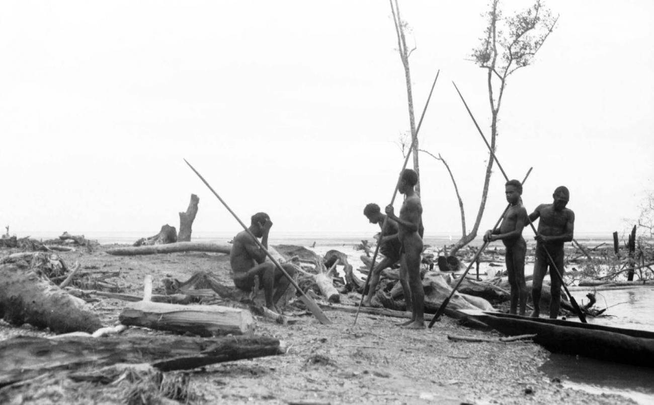 BD/133/69 - 
Tocht Merauke-Kapi: Mannen aan de oever van de rivier bij aangespoeld hout
