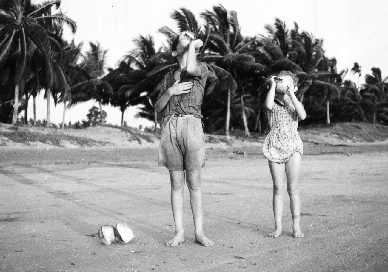 BD/133/833 - 
Westerse kinderen drinken kokosnootmelk op het strand
