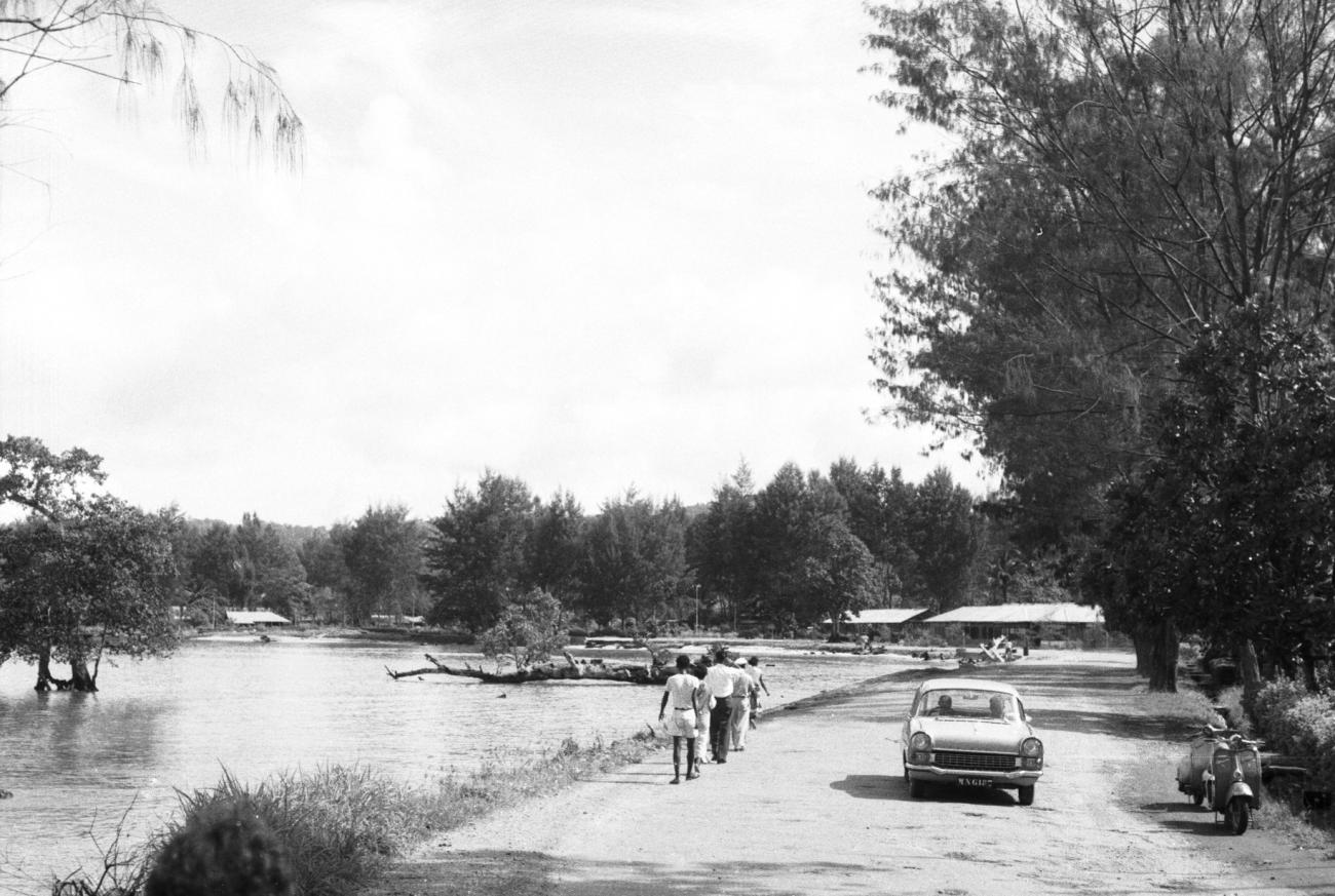 BD/133/900 - 
Straatbeeld van weg langs rivier, met mensen en auto 
