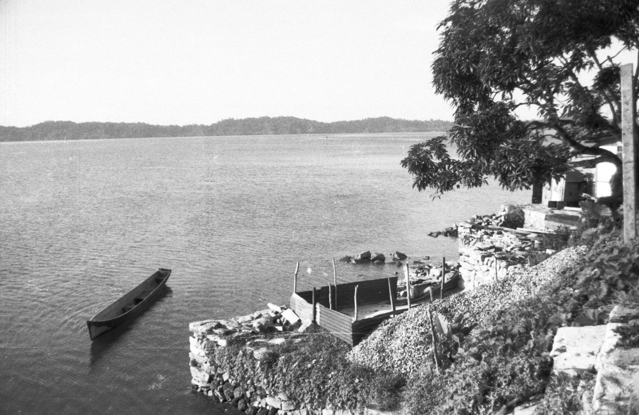 BD/133/919 - 
Prauw in het water bij nederzetting aan een baai
