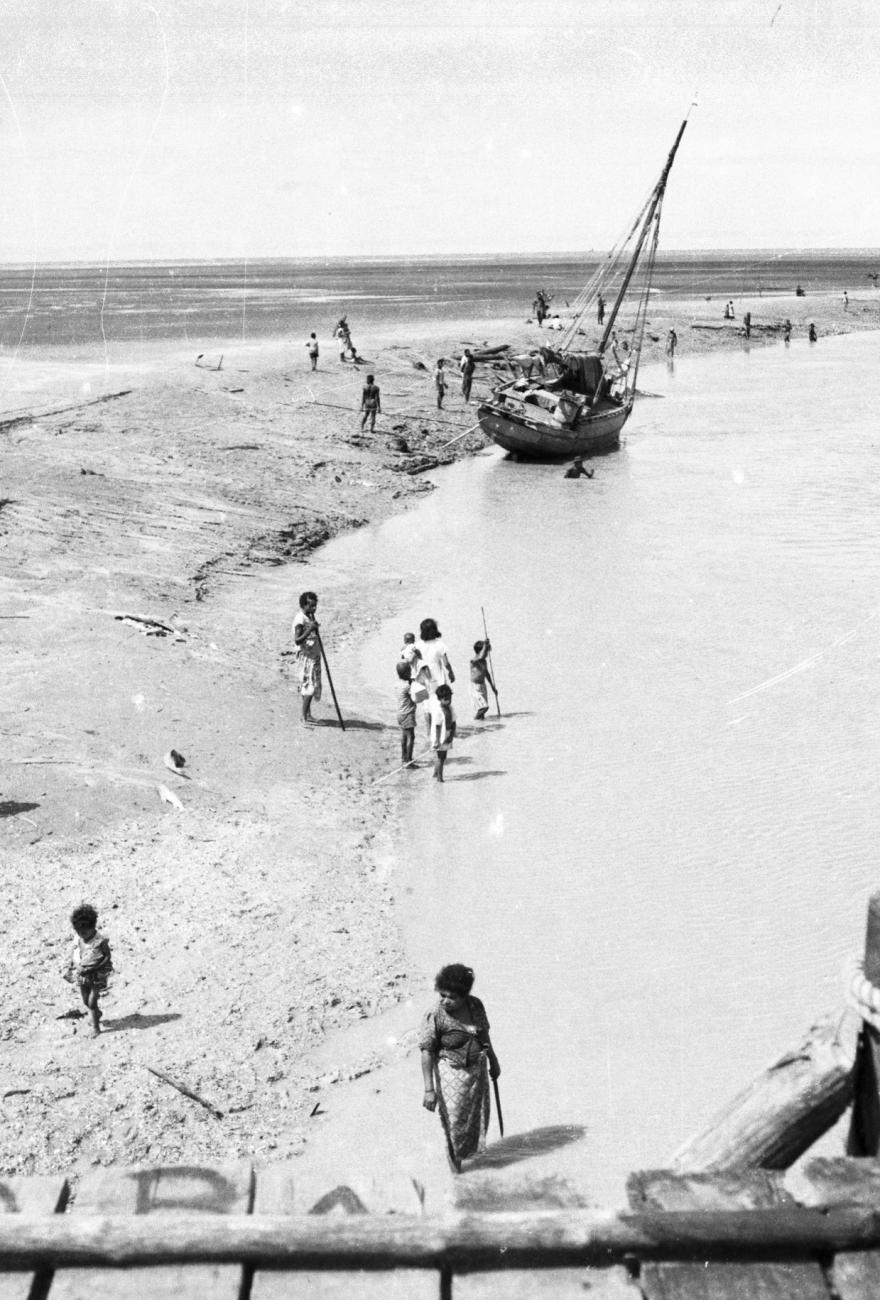 BD/133/948 - 
Getijdelandschap met met drooggevallen zeilschip en langs de oevers vissende Papoea&#039;s 
