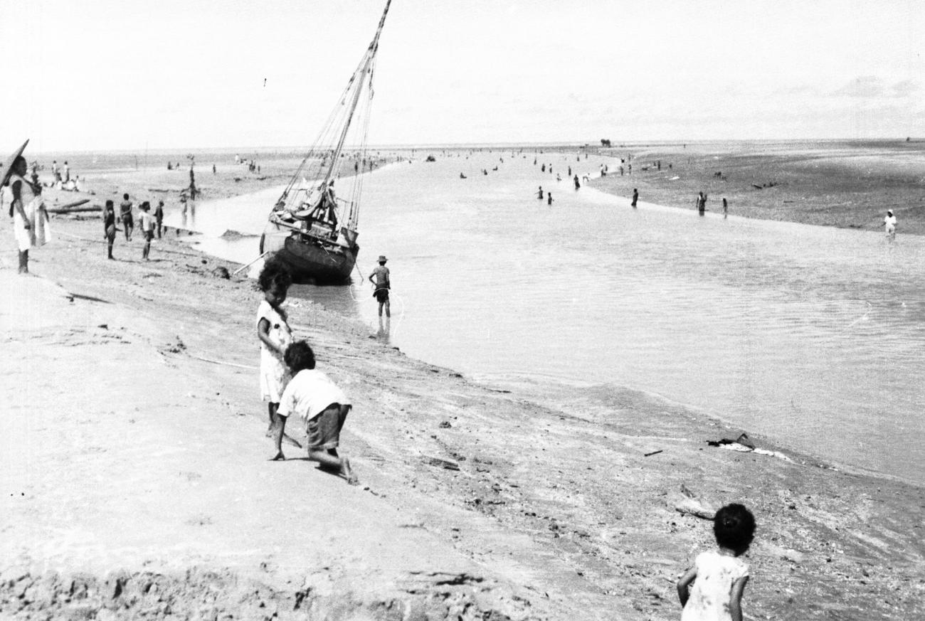 BD/133/950 - 
Getijdelandschap met met drooggevallen zeilschip en langs de oevers vissende Papoea&#039;s 
