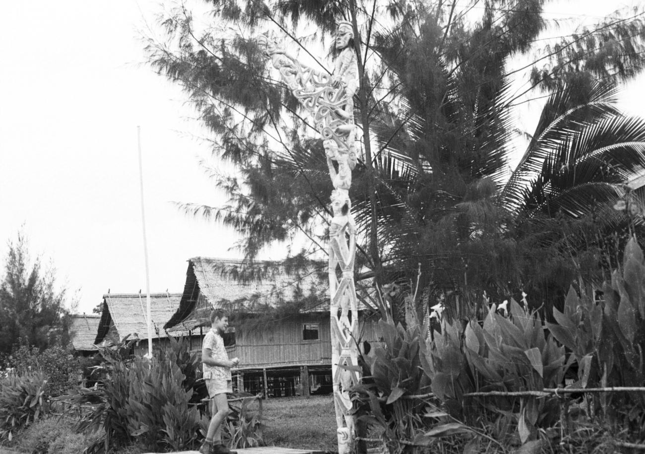 BD/133/967 - 
Westerse jongen bij Bisj-paal met traditionele huizen op de achtergrond
