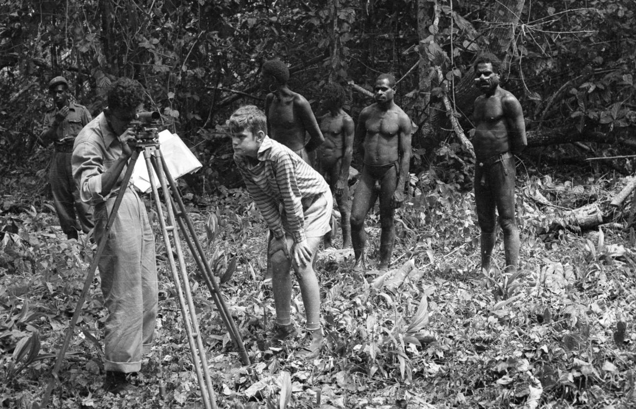 BD/133/985 - 
Landmeetkundige met westerse jongen, politieman en Papoea&#039;s (Asmat) in het oerwoud 
