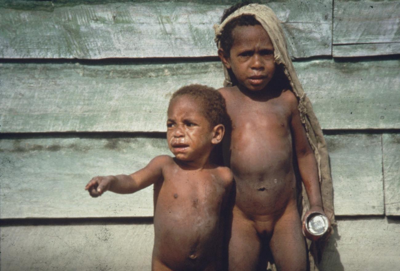BD/285/33 - 
Twee Ekari-jongetjes waarvan een met een grote lap stof in het haar en blikje in de hand
