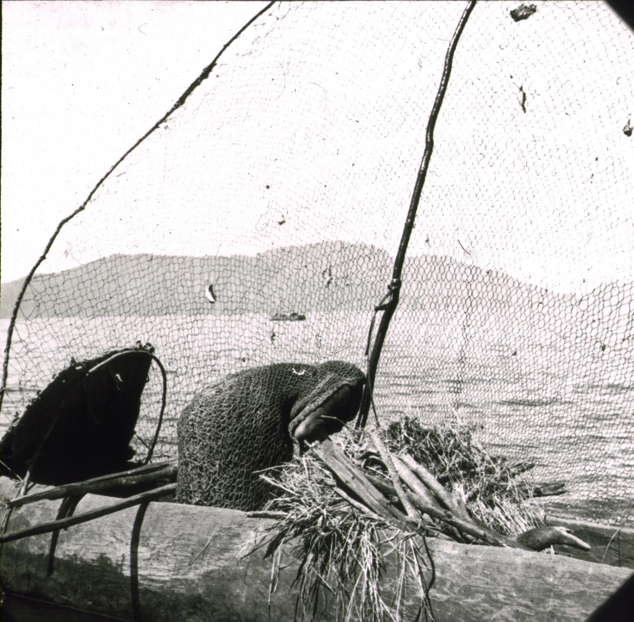 BD/329/16 - 
Papoea  in de weer met een visnet, varend in een prauw op een meer 

