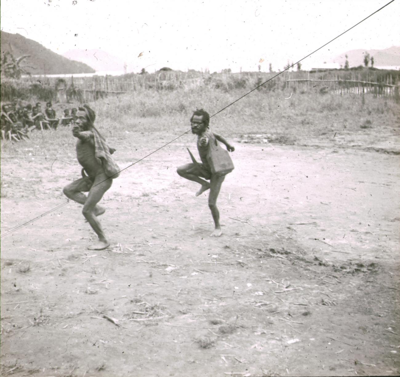 BD/329/40 - 
Twee Papoea-mannen voeren een dans uit onder toezien van stamgenoten
