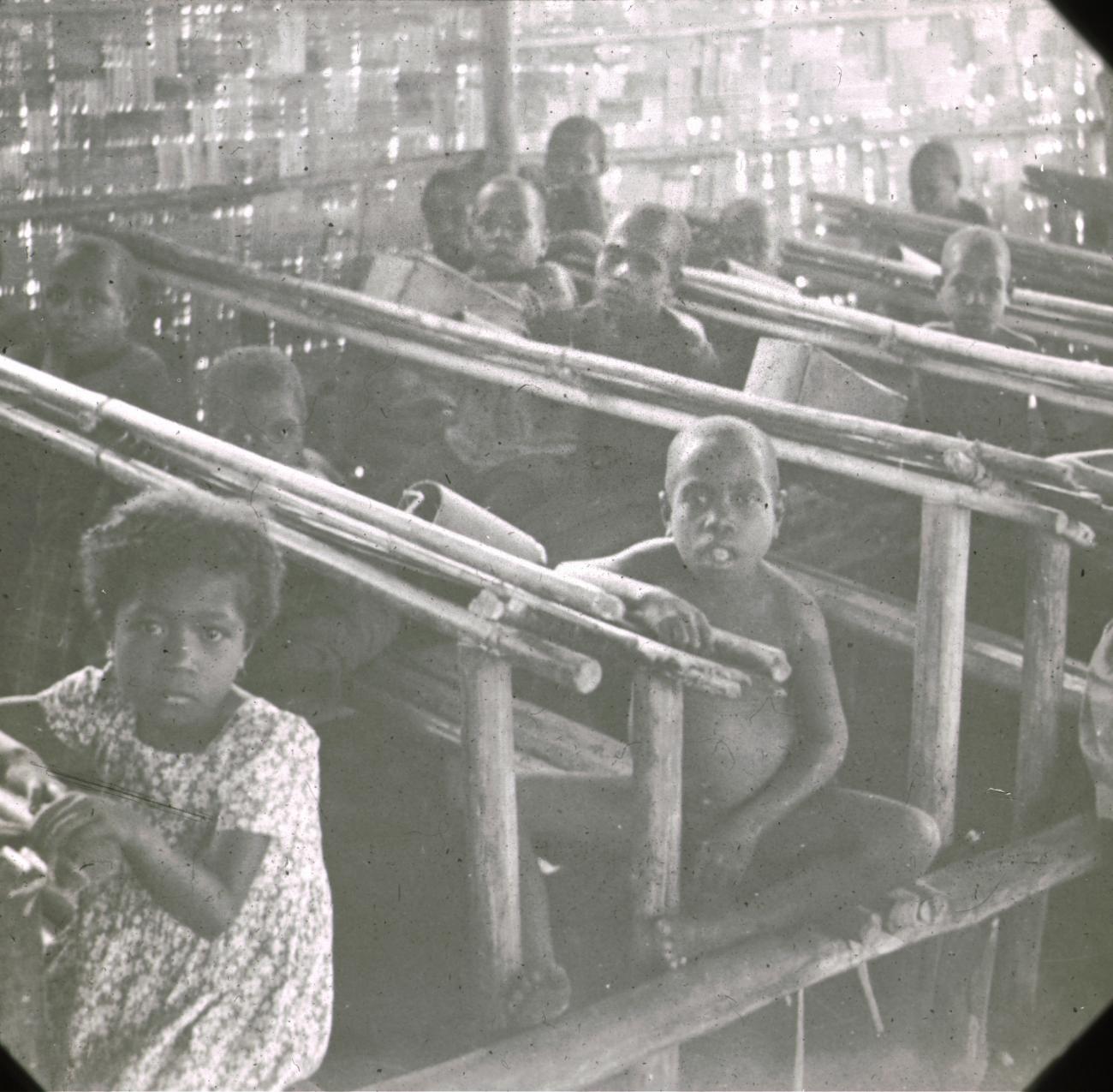BD/329/9 - 
Papoea-kinderen in de schoolbanken van een plattelandsschooltje

