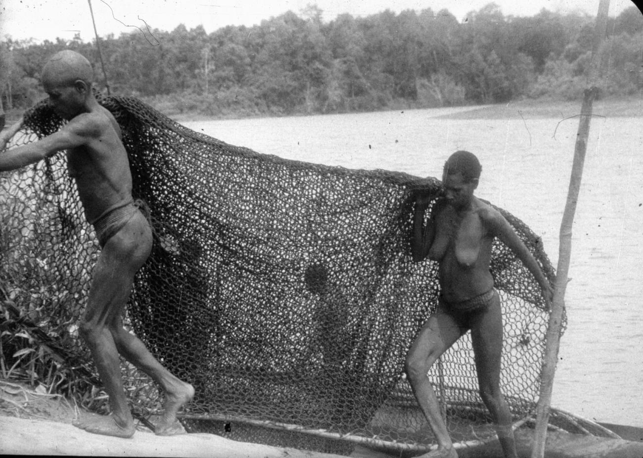 BD/216/227 - 
Vrouwen dragen visnet uit de prauw de rivieroever op
