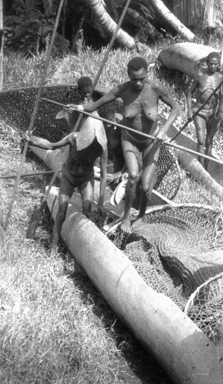 BD/216/232 - 
Vrouwen met peddels en visnetten in prauwen die op de oever zijn getrokken 
