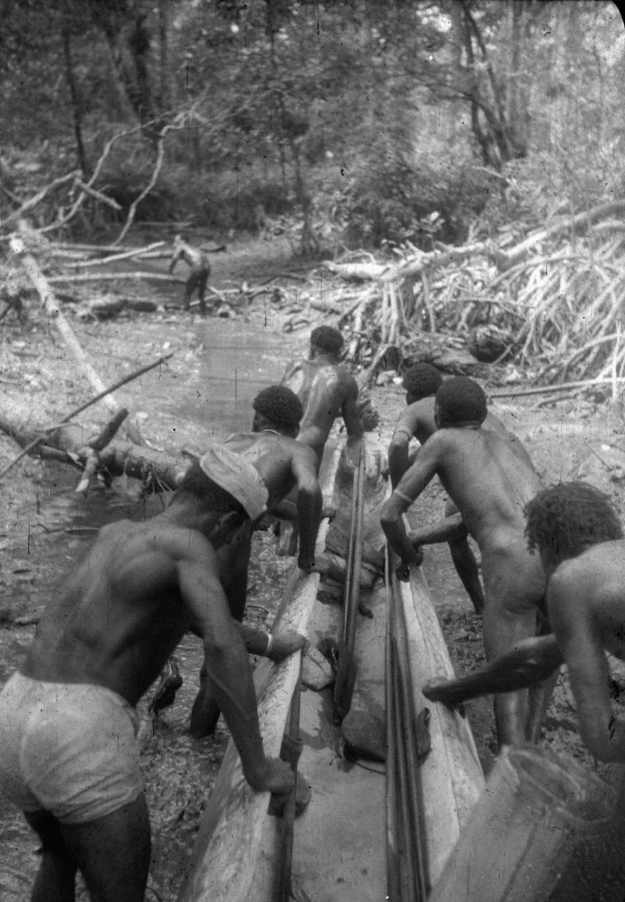 BD/216/235 - 
Mannen vervoeren prauw over een drooggevallen stuk rivier
