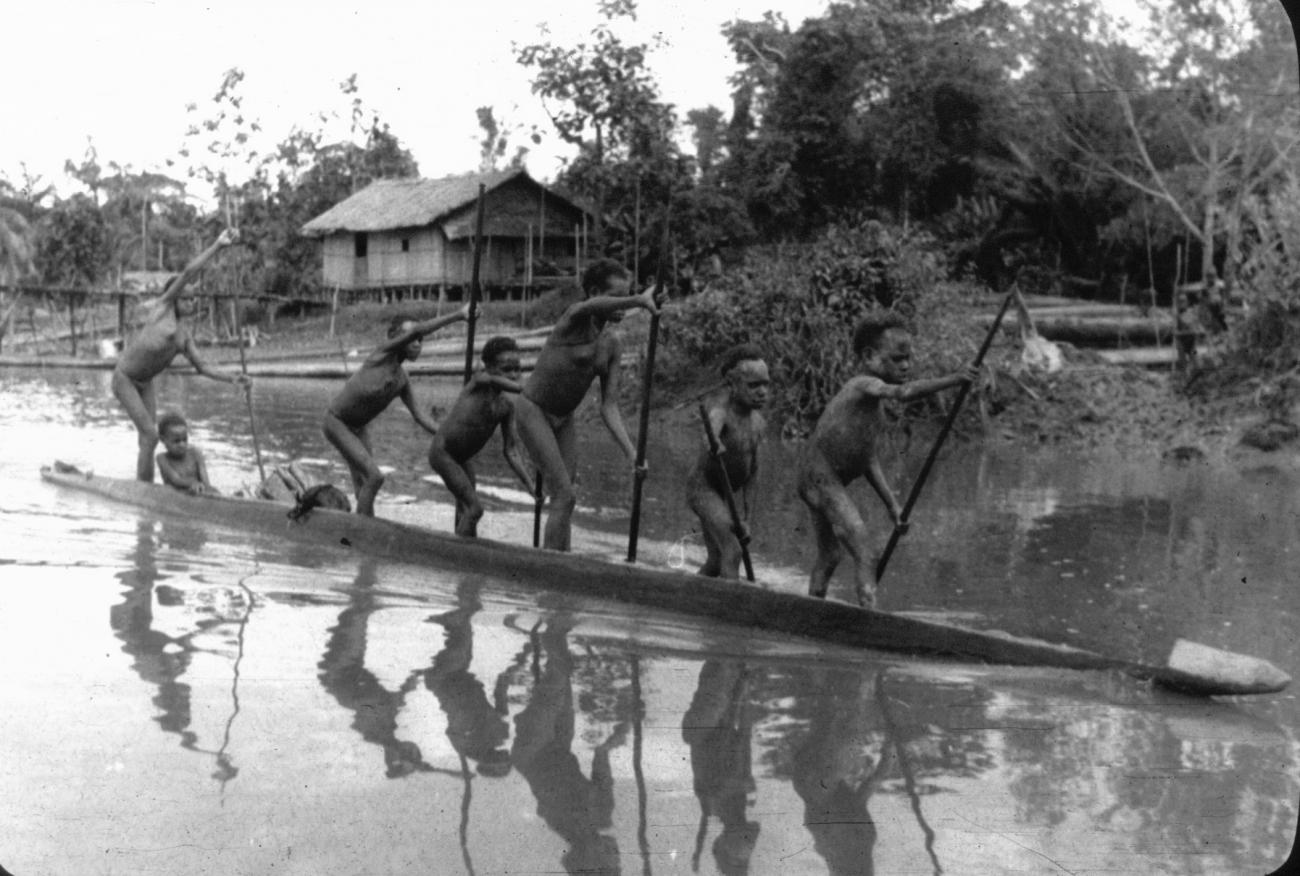 BD/216/247 - 
Jonge Asmatters met prauw op rivier met zicht op rivieroever en paalwoning
