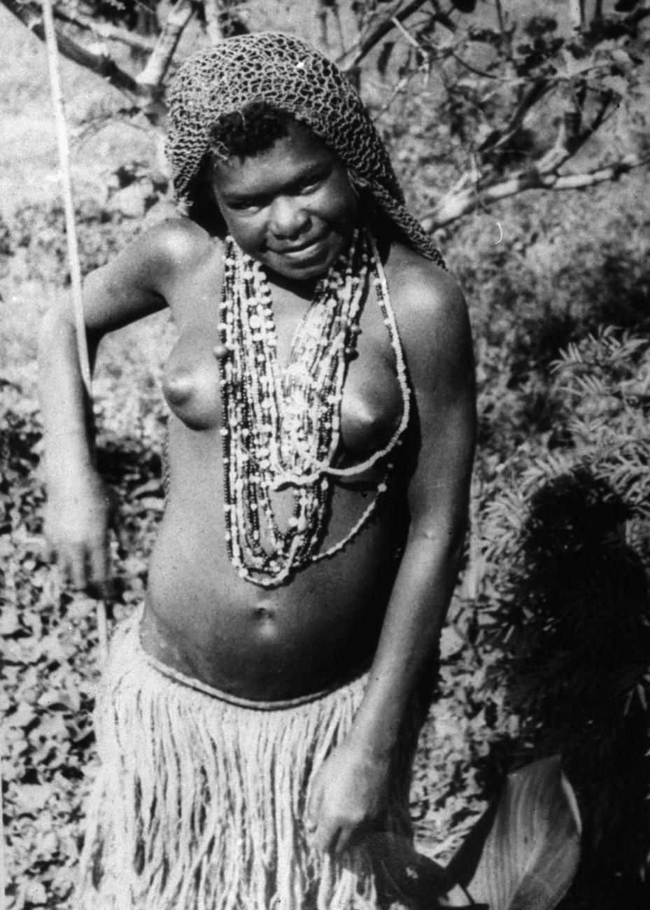 BD/216/89 - 
 Een Ekari meisje met rieten rok, ketting met kralenen zaden en haarnet
