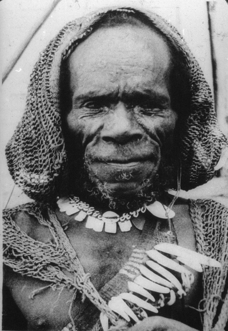 BD/216/90 - 
Een Ekari man met haarnet, halsketting van schelpen en draagnet met varkenstanden
