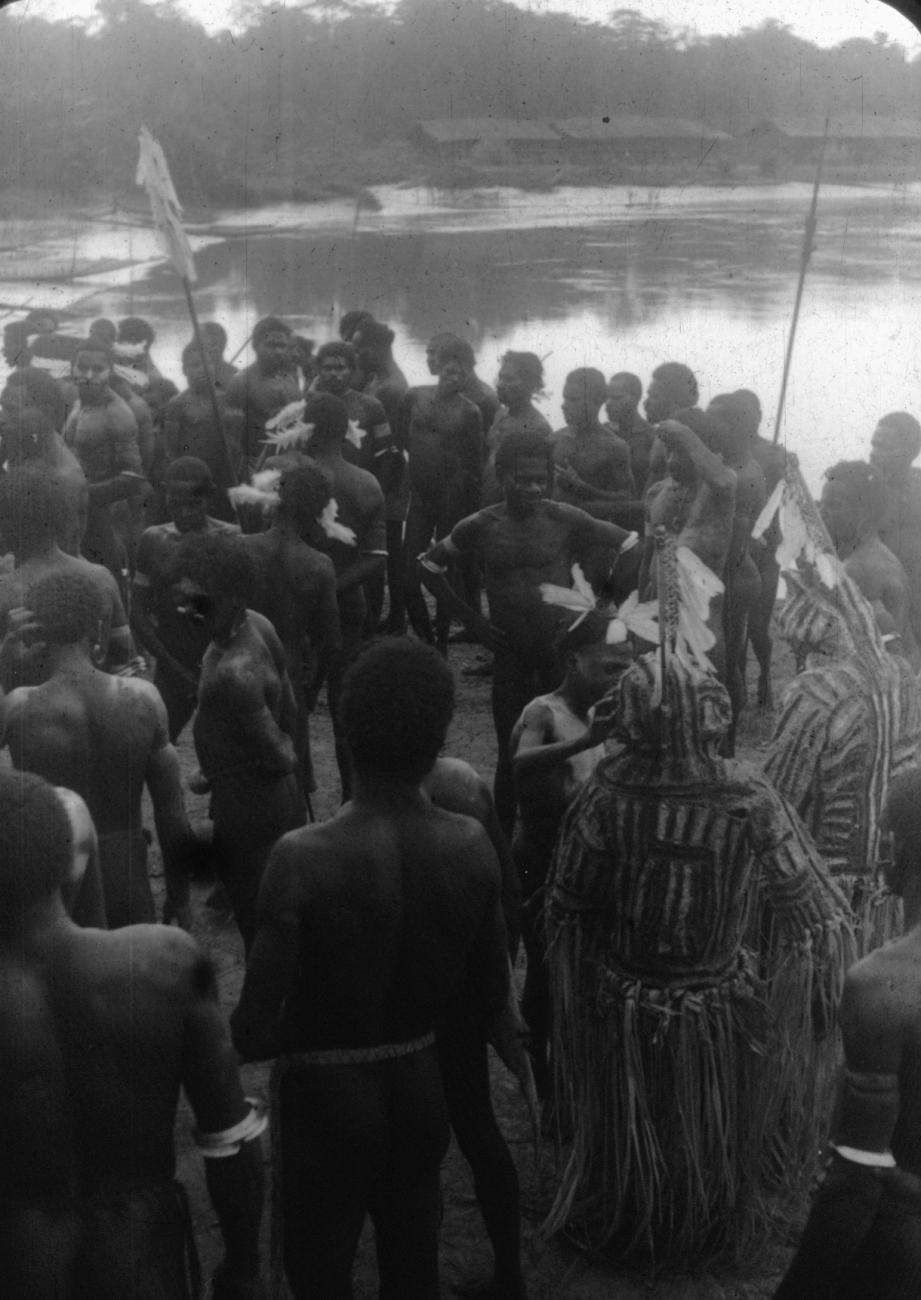 BD/216/97 - 
Groep mannen waarvan twee met Jipae kostuum dansmasker aan de rivieroever
