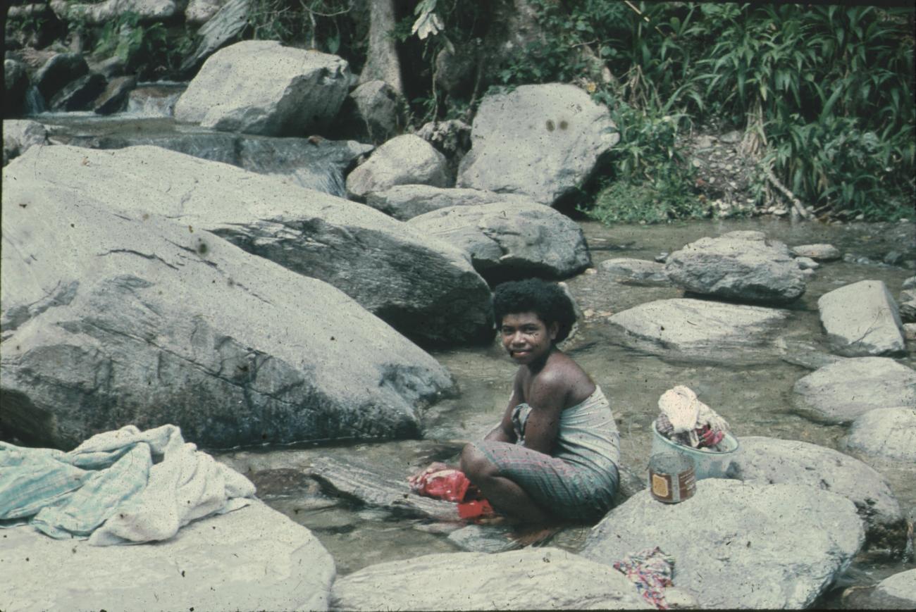 BD/248/206 - 
Een vrouw die kleren wast in het water tussen de stenen (kust NG)
