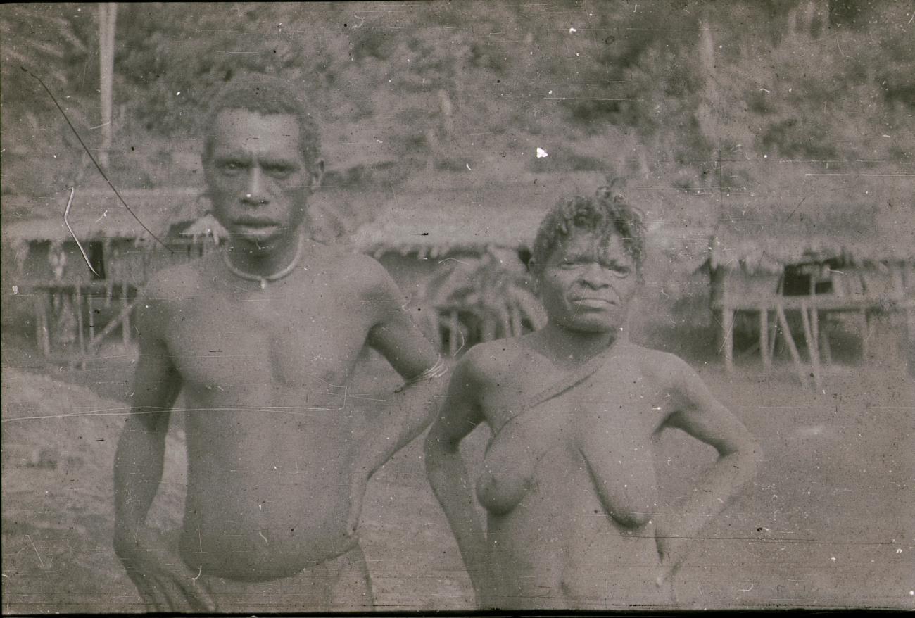 BD/309/194 - 
Man en vrouw met op de achtergrond traditionele paalwoningen
