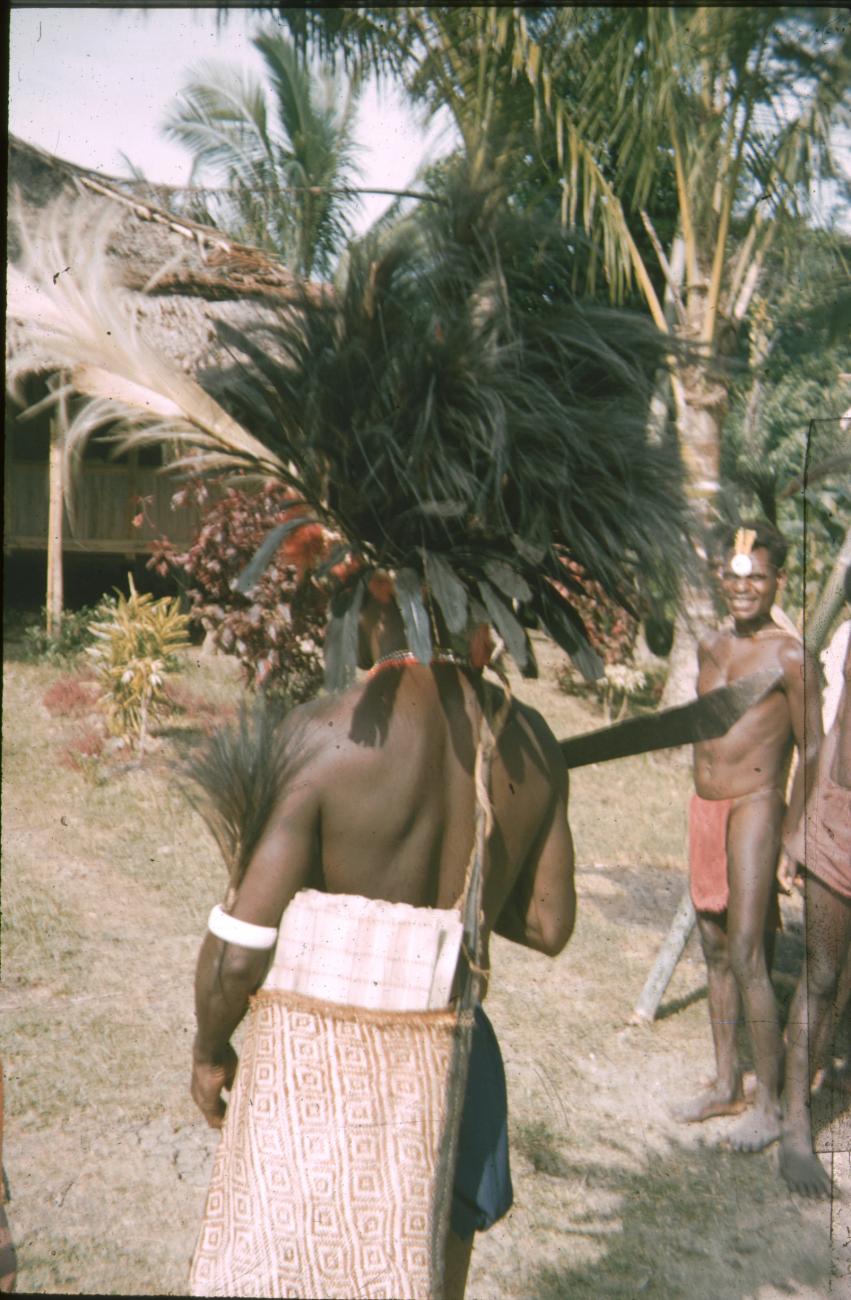 BD/309/257 - 
Man traditioneel uitgedost met hoofdtooi, tas, neusversiering en machete
