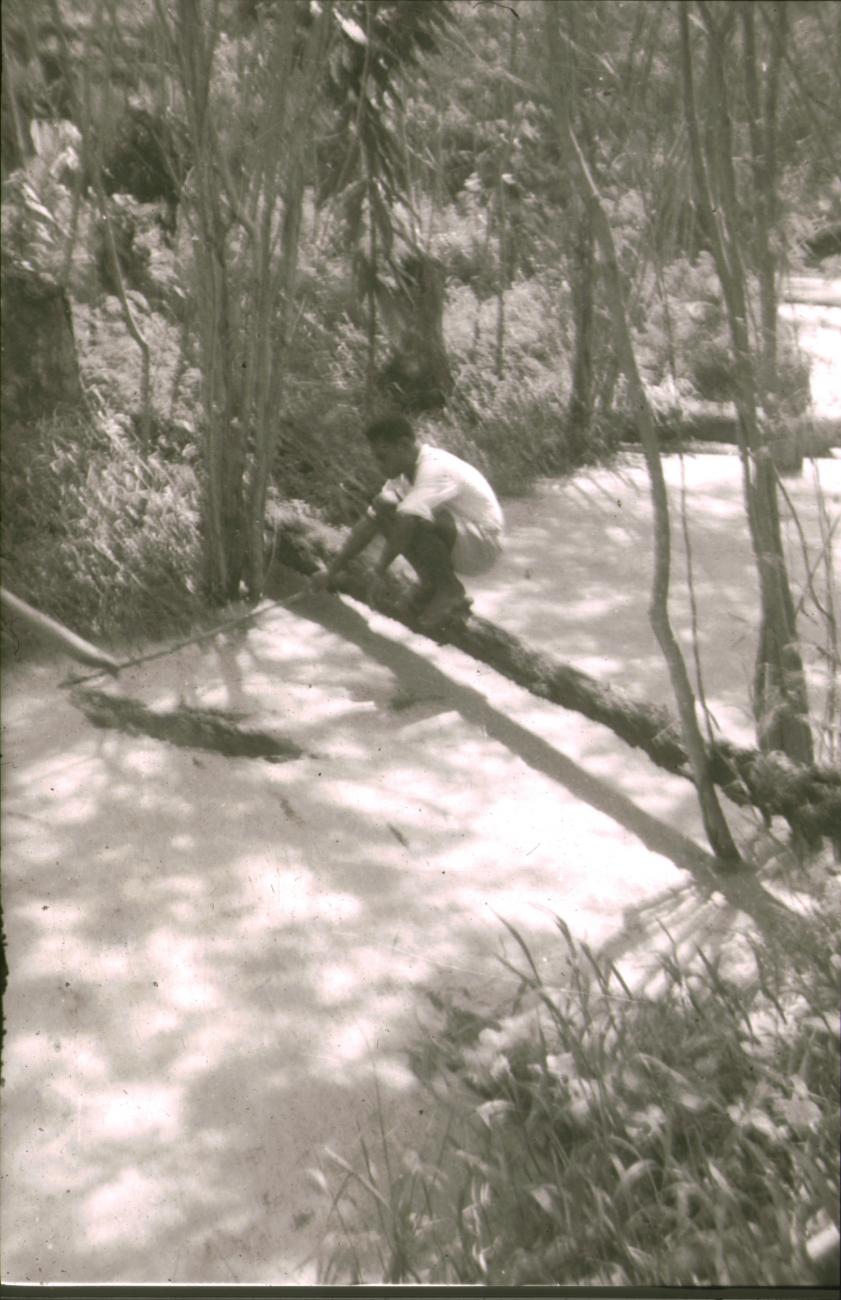 BD/309/314 - 
Man zittend op een boomstam die over het water ligt 
