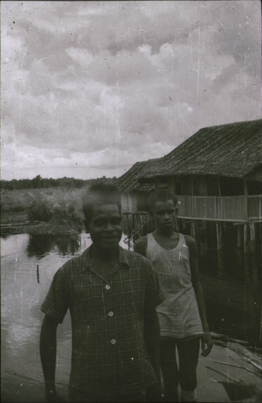 BD/309/347 - 
Twee mannen poseren bij water en paalwoningen
