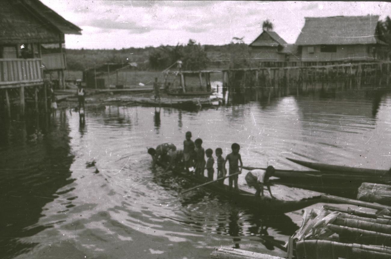 BD/309/348 - 
Dorp aan de rivier met paalwoningen en kinderen in een prauw
