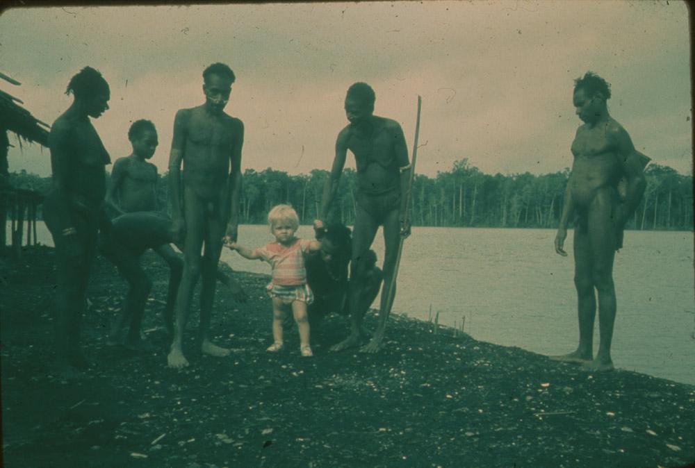 BD/30/59 - 
Asmat women and men with a small white child at the river shore
