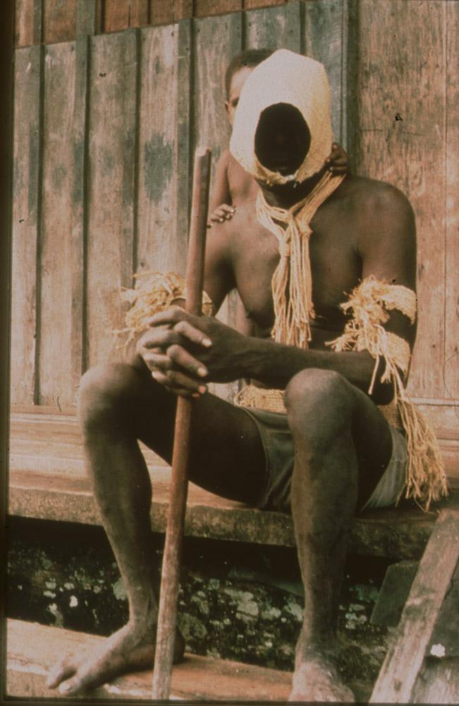 BD/30/76 - 
Asmat man in mourning cloths sitting on stairs with a child behind him
