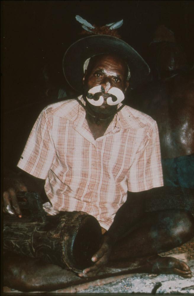 BD/30/88 - 
Asmat man sitting with drum, hat and nose decoration
