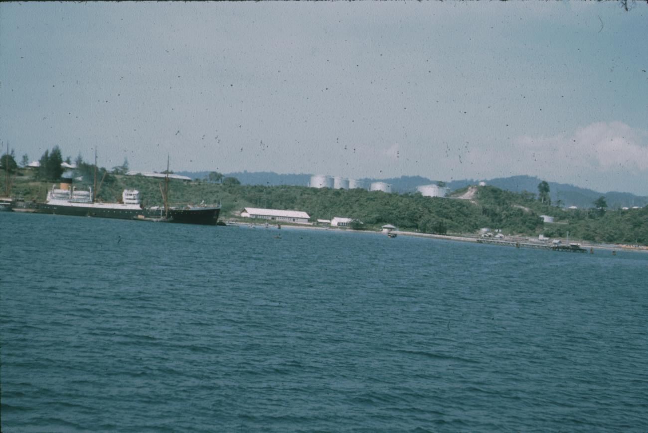 BD/171/480 - 
Vrachtschip in haven, reservoirs op achtergrond.
